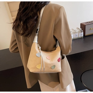 Model view of a beige suede hobo bag with colorful heart patches and silver shoulder strap