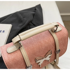 Close-up of pink suede crossbody bag featuring a silver butterfly buckle and white handle