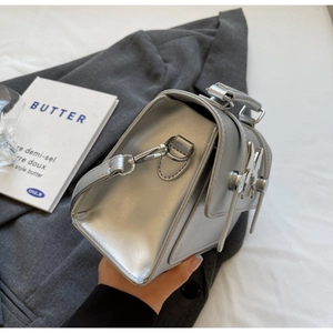 Détail d'un sac argenté mat avec ornement lapin en métal sur fond de tissu gris