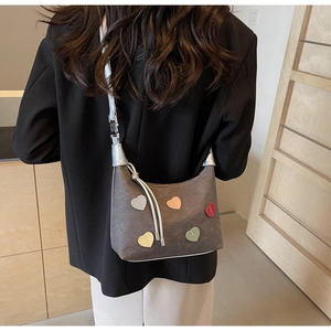 Detail of grey crossbody bag with colorful heart patches on model in black blazer