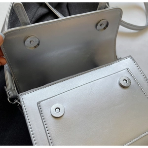 Détail du sac à bandoulière argenté montrant la double fermeture magnétique et les coutures
