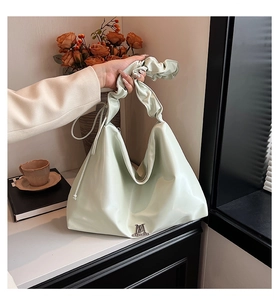 Detail der mintgrünen Tragetasche mit Faltenhebel und silbernem M-Logo im Lifestyle-Stil
