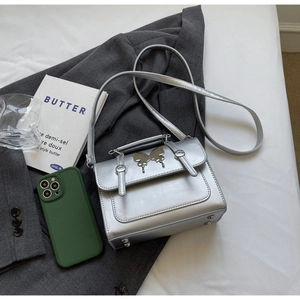 Détail du mini sac argenté Y2K avec ornement papillon en métal sur un blazer gris
