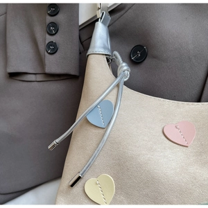 Detailed shot of beige leather handbag featuring colorful stitched heart patches and silver hardware