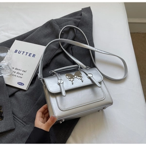 Détail d'un sac carré argenté métallisé avec ornement papillon sur un blazer gris