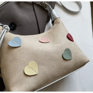 Close-up of beige handbag featuring colorful heart patches and silver metallic details
