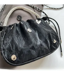 Detail of black pleated handbag featuring beaded handle and silver heart hardware
