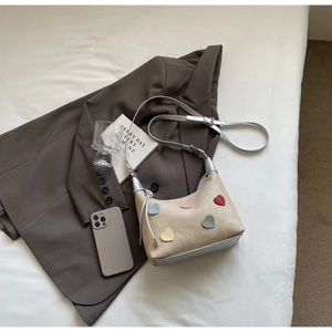 Flat lay of beige dumpling bag with colorful heart patches and silver strap on a grey suit