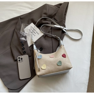 Detail of beige suede handbag with colorful stitched hearts and silver leather strap
