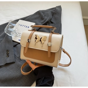 Détail du sac bandoulière avec fermoir papillon en métal sur cuir beige et marron