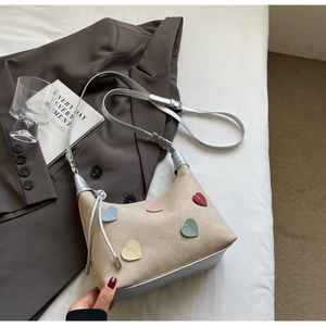 Flat lay of heart-patterned beige suede dumpling bag with silver metallic straps and accents