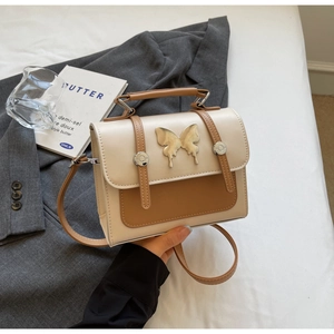 Détail du sac bandoulière bicolore avec ornement papillon en métal et boucles