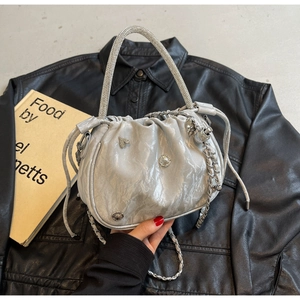 Close-up of pleated silver handbag with crystal-embellished handle and metallic charms