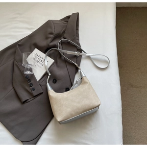 Detail of beige suede crescent bag over brown blazer with silver metallic strap accents