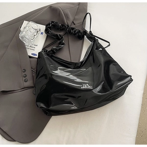 Detail der schwarzen Lackleder-Hobo-Tasche mit gerafftem Riemen auf grauem Blazer
