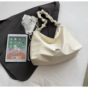 Detail der cremeweißen Leder-Tote-Bag mit Scrunchie-Riemen und Logo-Akzent aus Metall
