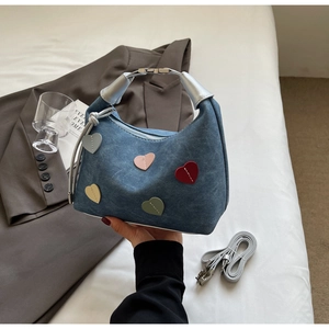 Detail of blue denim hobo bag with colorful heart patches and silver metal buckles