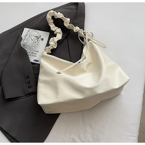 Detail der cremeweißen Falten-Umhängetasche mit geknotetem Träger auf dunklem Blazer