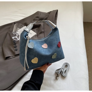 Detail of blue denim bag with colorful heart patches and silver top handle on a white desk
