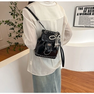 Detail of glossy black bucket backpack with silver chain and pearl bow charm accessory