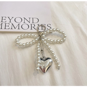 Detail of a pearl bow bag charm with a silver heart pendant on a textured white fabric