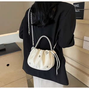 Detail of cream pleated bucket bag with rhinestone handle and metal chain strap on model