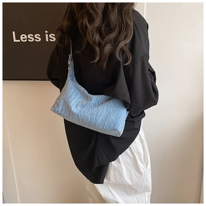 Close-up of light blue textured denim shoulder bag worn by model against minimalist background