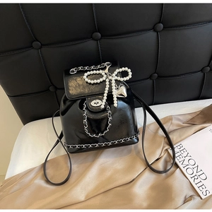 Detail of glossy black chain backpack with pearl bow charm and silver metallic buckle