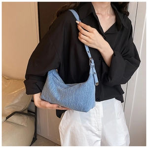 Close-up of light blue denim hobo bag with adjustable strap worn on woman's shoulder