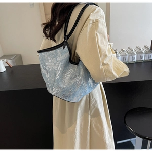 Detail der blauen Denim-Tragetasche mit silbernen Pailletten und schwarzen Lederriemen am Model