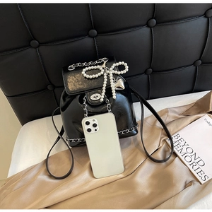 Detail of black glossy mini backpack with pearl bow, heart charm and phone for size
