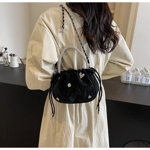 Detail of black velvet bucket bag with rhinestone heart and chain strap on table
