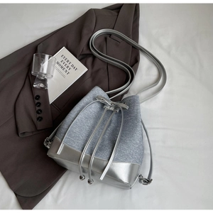 Detail of silver contrast color bucket bag with drawstring closure on white fabric