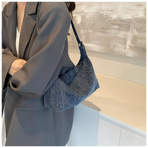 Detailed texture of blue denim crescent bag with zipper closure on a stylish model