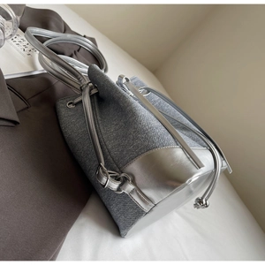 Macro view of grey fabric bucket bag with silver leather base and shiny drawstring closure