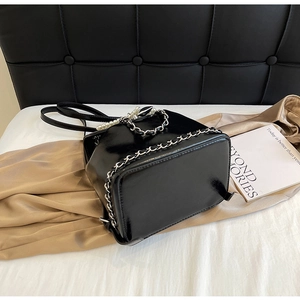 Detail of glossy black patent leather bucket bag with pearl handle and metal chain decoration
