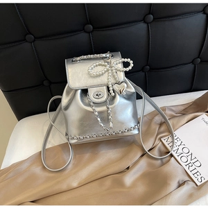 Detail of silver metallic backpack with pearl bow, heart pendant and chain accents