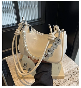 Creamy white crescent handbag with pearl and heart chain details on marble background