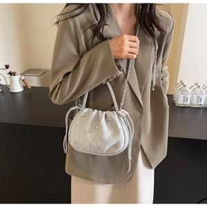 Detail of silver pleated bucket bag with rhinestone handle and crystal charms on a model