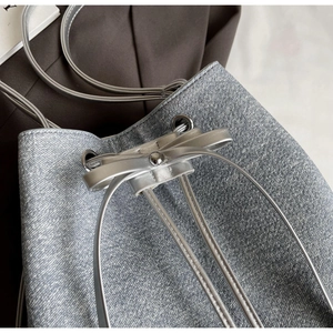 Detail of silver bucket bag showing textured fabric, drawstring closure, and metal eyelets