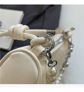 Detail of off-white textured leather bag with metallic clasp and large pearl ornament
