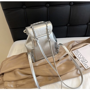 Detail of silver metallic backpack featuring a faux pearl handle and chic chain straps
