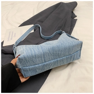Detail of light blue denim shoulder bag featuring silver rivets and wide strap