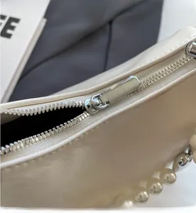 Detailed close-up of smooth silver zipper and elegant pearl handle on white leather bag