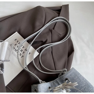 Detailed view of silver drawstring bucket bag on brown suit with elegant props