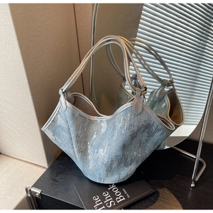Detail der hellblauen Denim-Tote mit silbernen Pailletten und grauen Ledergriffen auf Schwarz