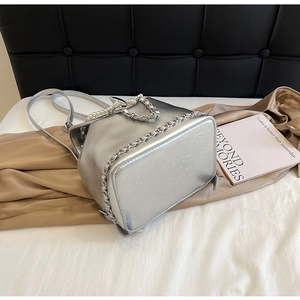 Detail of silver metallic bucket bag with pearl handle and chain straps on satin background