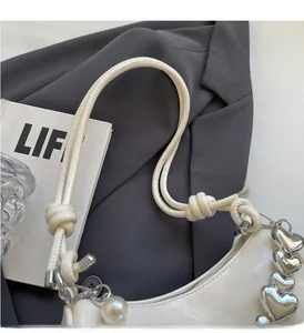 Detail of white half-moon bag with knot strap, silver heart charm and pearl drop
