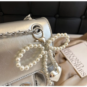 Detail of silver metallic textured bag with pearl bow and heart charm on chain strap