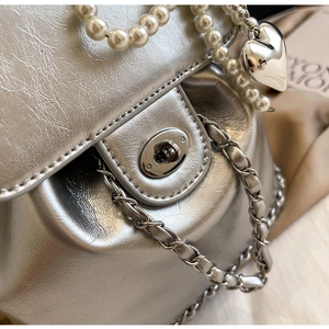 Detail of silver chain bag with white pearl strap, metal heart pendant and polished clasp